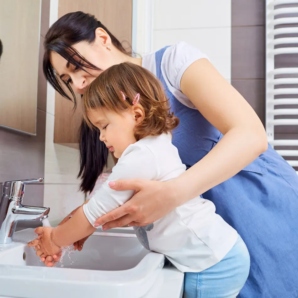 A woman and a child washing their hands at a sink, promoting hygiene and cleanliness.